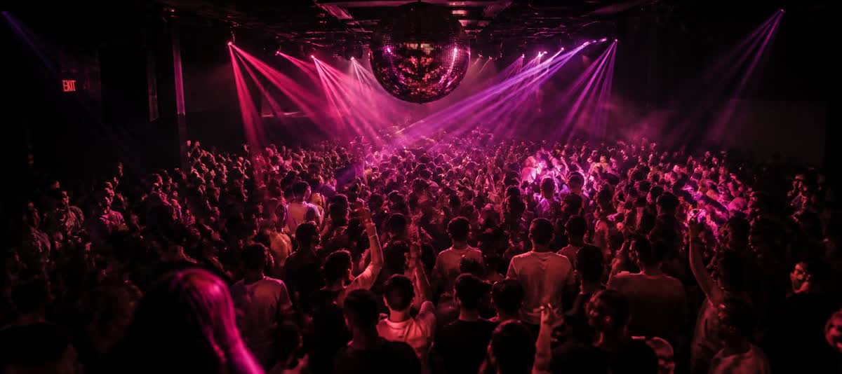 Packed dance floor under a disco ball and pink lasers